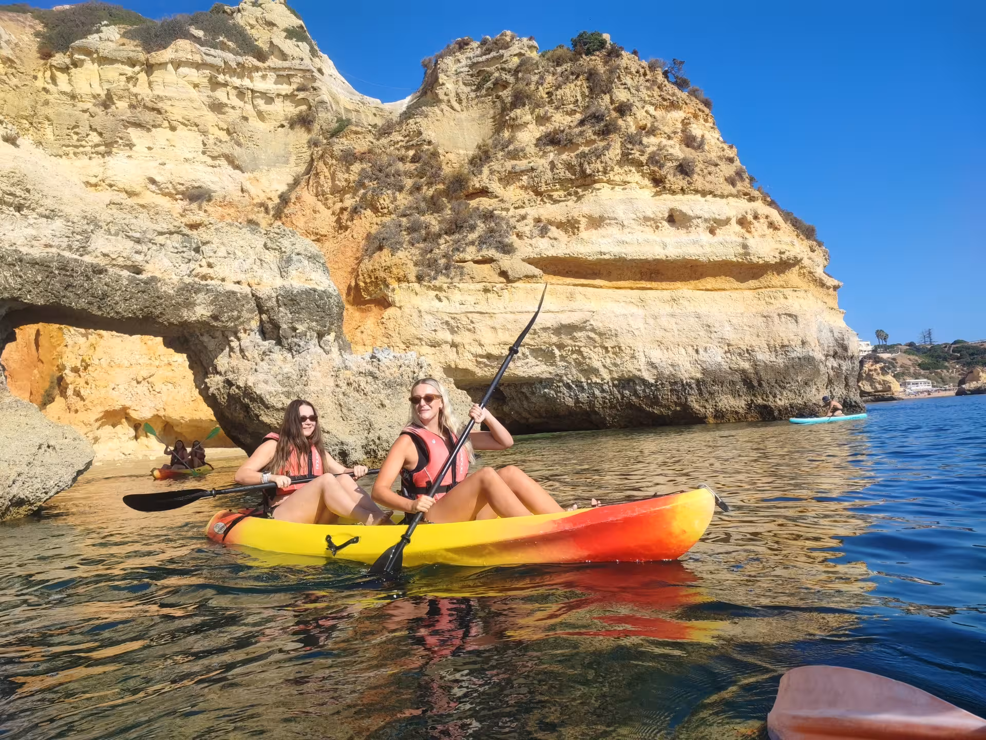 Two friends paddle a double kayak along Algarve sea caves and golden cliffs on a sunny Portugal coastal adventure tour