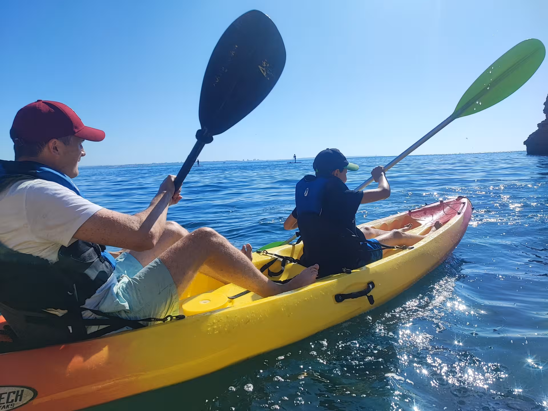Two people paddling a bright double kayak on calm blue sea during a sunny coastal adventure tour