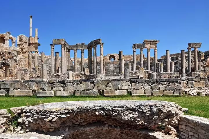 Panoramic view of Dougga's Roman ruins in Tunisia, featuring prominent stone columns against a vibrant blue sky.