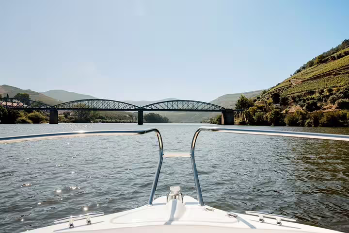 View from a luxury boat on the Douro River approaching a picturesque bridge under clear blue skies.