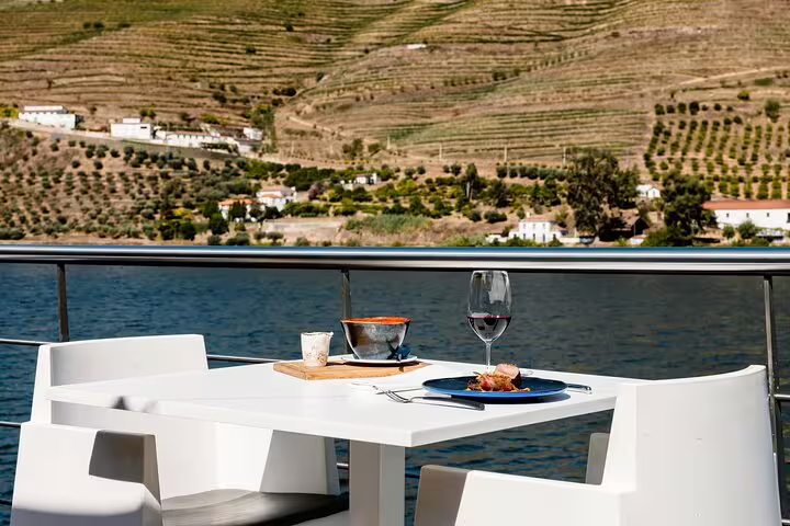 Elegant riverside dining setup on a Douro private cruise, featuring gourmet dishes and wine with vineyard views.
