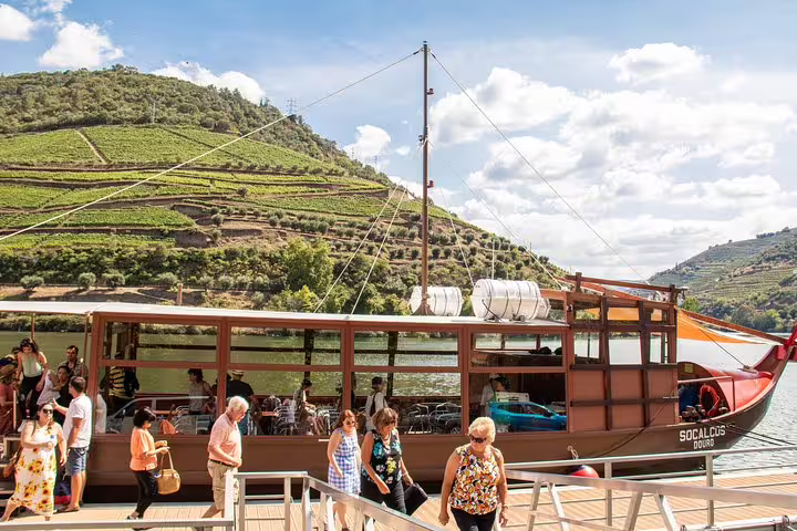 Tourists disembark from a traditional wooden boat after a scenic Douro River cruise past picturesque vineyards.