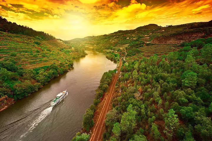 A cruise ship sails along the picturesque Douro River at sunset, surrounded by lush vineyards and hills near Pinhão.