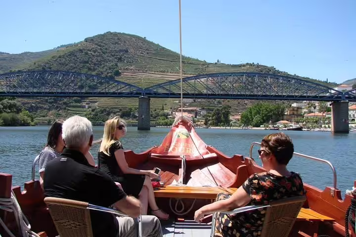Visitors relaxing on a traditional boat cruise along the Douro River, passing under a picturesque bridge with hillside vineyards.