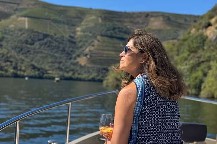 Guest enjoying Douro River private boat cruise with wine glass, luxury Douro Valley tour and vineyard views