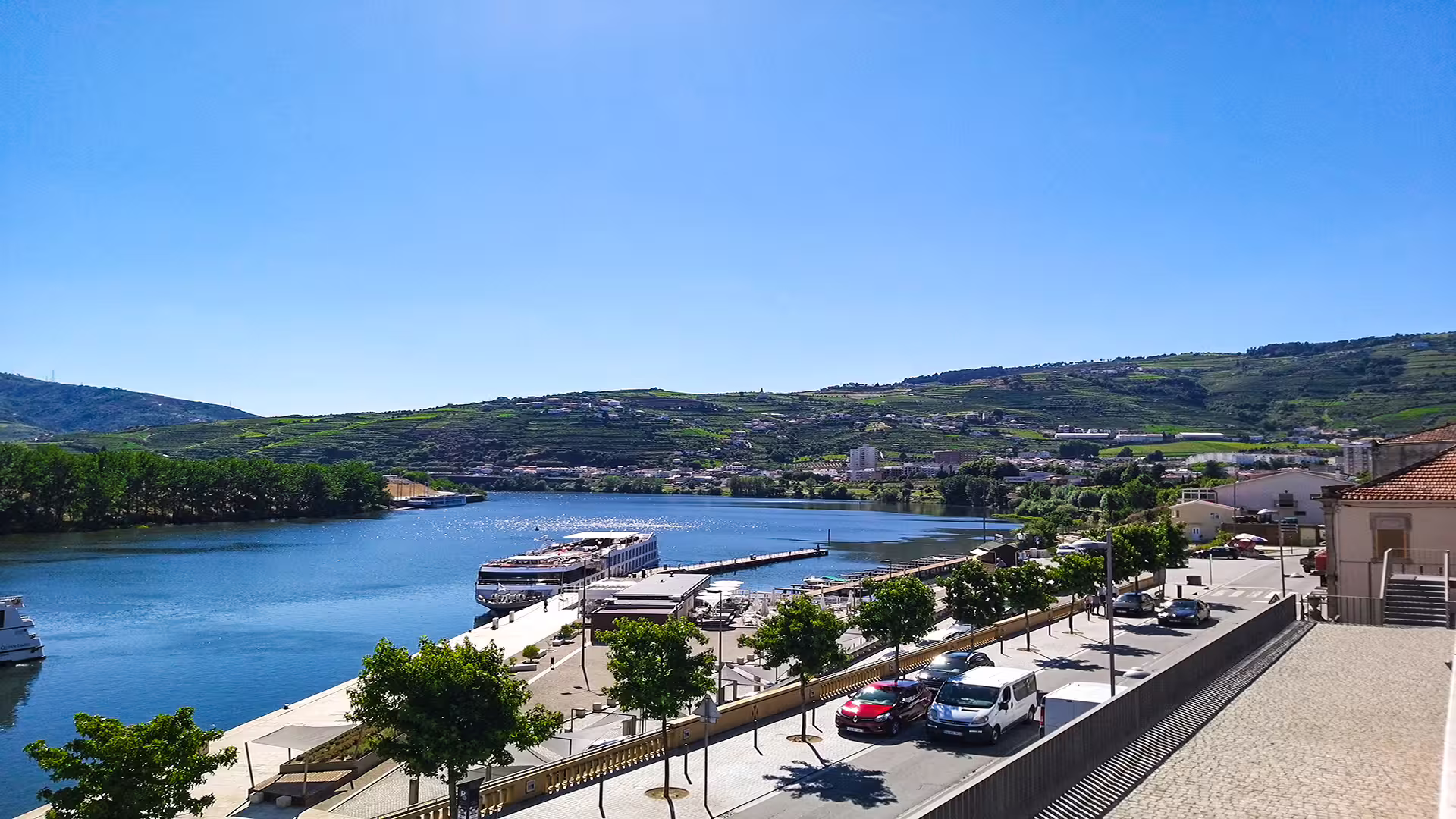 Scenic view of the Douro River with boats, lush hills, and charming village, highlighting the beauty of the Foz Côa region.