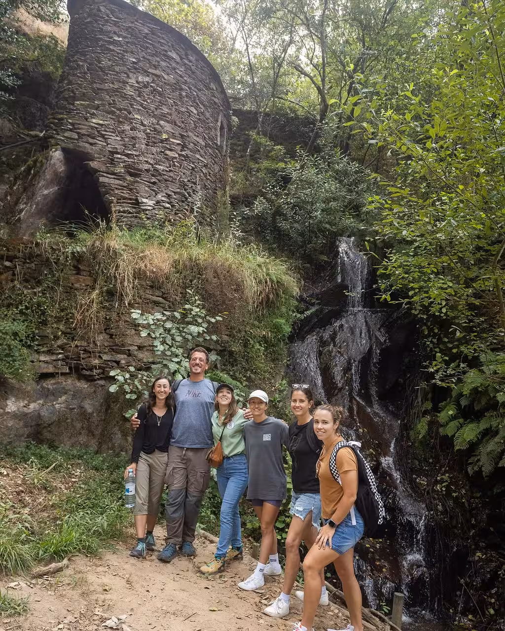 Group at a hidden waterfall by an old stone mill, Douro River vintage car tour to secret gems in Portugal