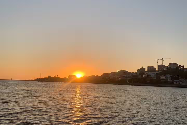 Golden sunset over the Douro River in Porto, viewed from a sailboat, with city skyline silhouetted against the sky.