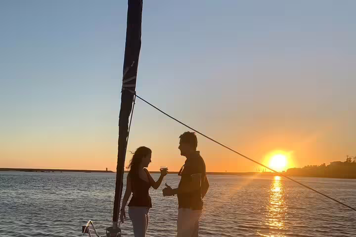 Couple enjoys a romantic Douro River sunset sailboat experience in Porto, surrounded by serene waters and vibrant sky.