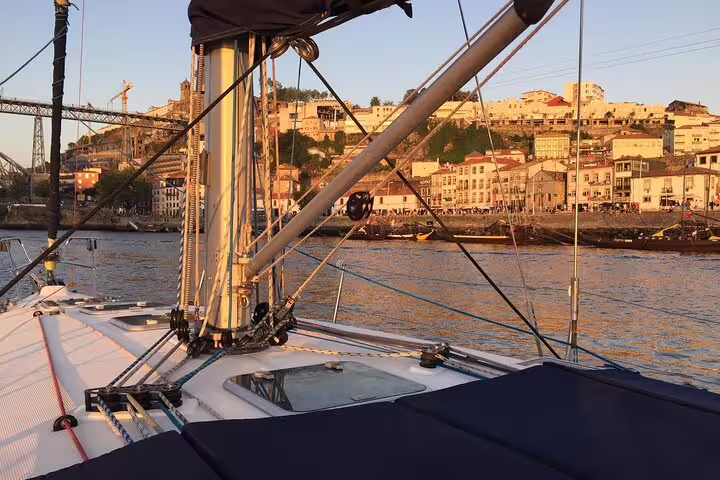 Sailboat deck on the Douro River at sunset with scenic views of Porto's historic buildings and Luis I Bridge in the background.