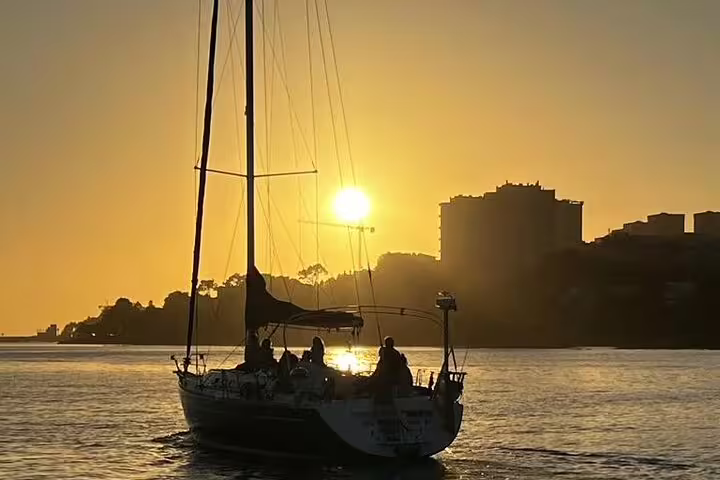 Sailboat glides on Douro River at sunset with Porto skyline silhouetted, offering a serene and picturesque sailing experience.