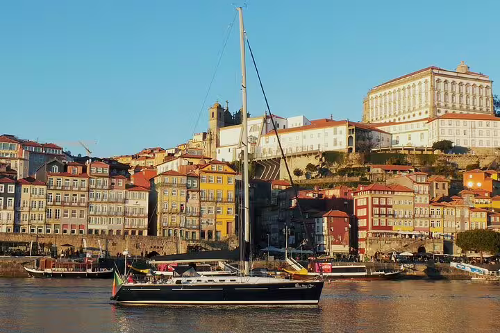 Sailboat gliding on Douro River at sunset with Porto's colorful historic buildings and vibrant skyline in the background.