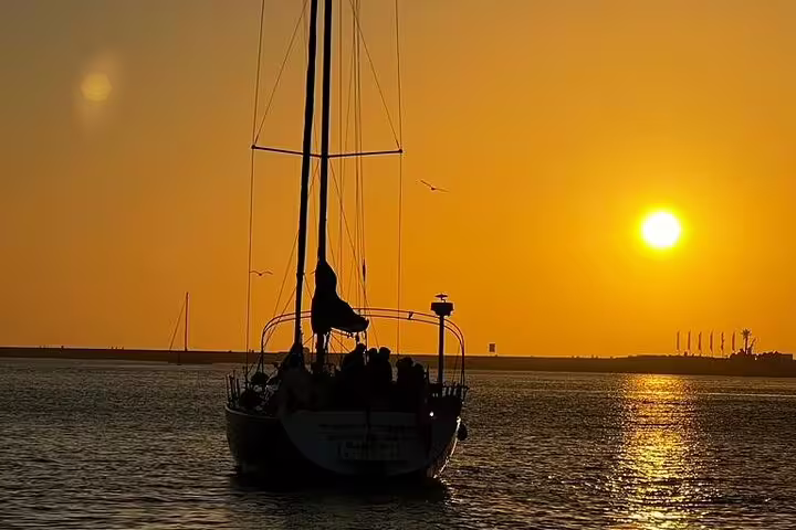 Sailboat gliding on the Douro River at sunset in Porto, offering a serene and picturesque experience with golden skies and calm waters.