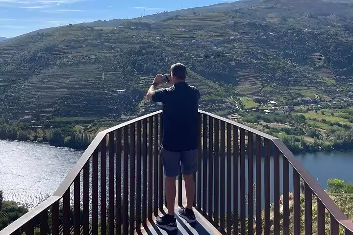 Tourist capturing stunning Douro Valley vineyard and river views from an elevated viewpoint.
