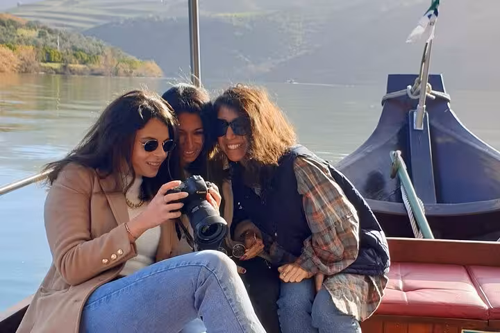Friends enjoy a Douro Valley boat tour, reviewing photos on deck with river views during wine tastings and lunch