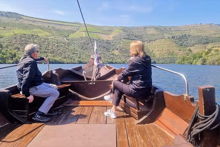 Guests relaxing on Douro River boat with views of terraced vineyards during private Douro Valley experience
