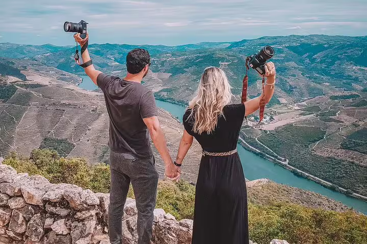 Couple holding cameras and overlooking the Douro River and vineyards, capturing the stunning landscape.
