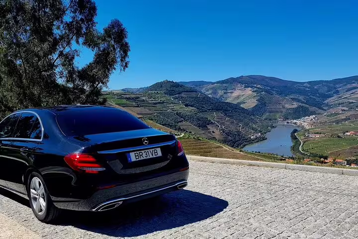 Luxury vehicle parked with panoramic view of Douro Valley vineyards and river under clear blue skies.