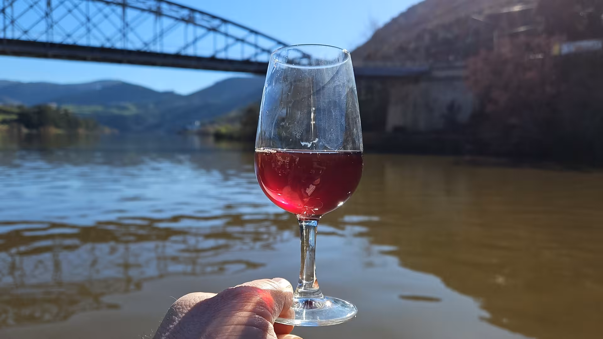 Glass of Douro red wine held over the river on a boat trip, perfect for Douro Valley wine tasting tour