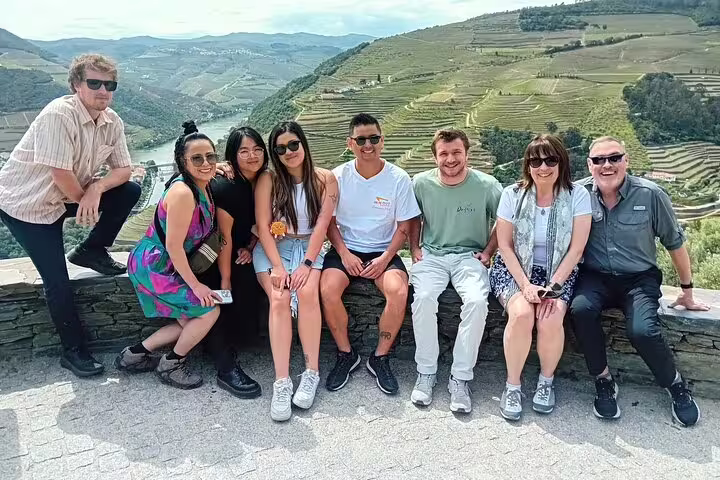 Visitors posing with panoramic views of Douro Valley's terraced vineyards on a vineyard tour.
