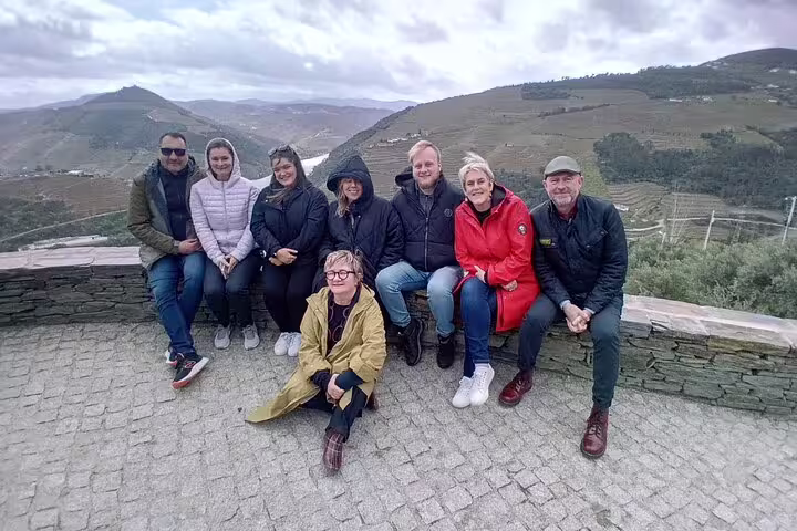 Group of tourists posing with stunning Douro Valley landscape backdrop on guided vineyard tour.