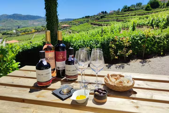 Scenic Douro vineyard with wine bottles, glasses, and local delicacies set on a wooden table for a tasting experience.