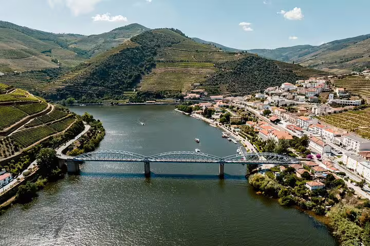 Aerial view of Douro Valley vineyards, river, and a historic village with a scenic bridge.