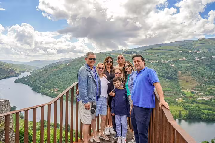 Group enjoying a scenic view of the Douro Valley vineyards and river during a private tour from Lisbon, under a cloudy sky.