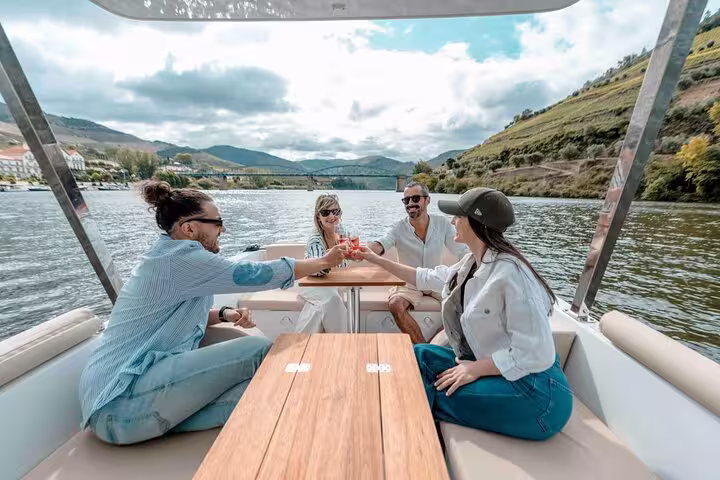 Group enjoying wine on a Douro Valley boat ride, with scenic vineyards in the background.
