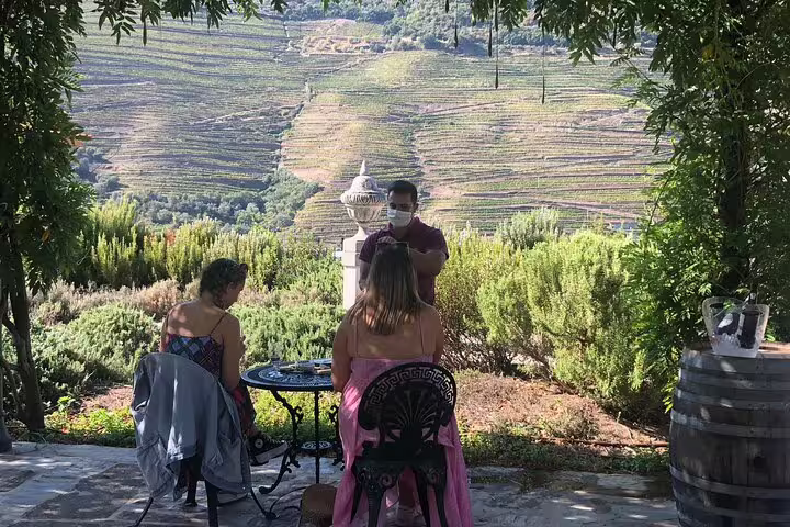 Guests seated outdoors at Douro Valley vineyard, savoring wine with scenic terrace views.