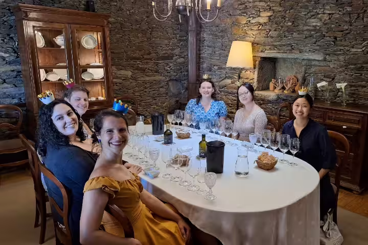 Guests enjoying a wine tasting in a rustic Douro Valley winery, seated at a table with glasses and snacks, showcasing a cozy ambiance.