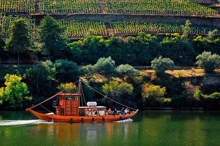 Traditional rabelo boat cruising Douro River past terraced vineyards on private Douro Valley wine tour from Porto