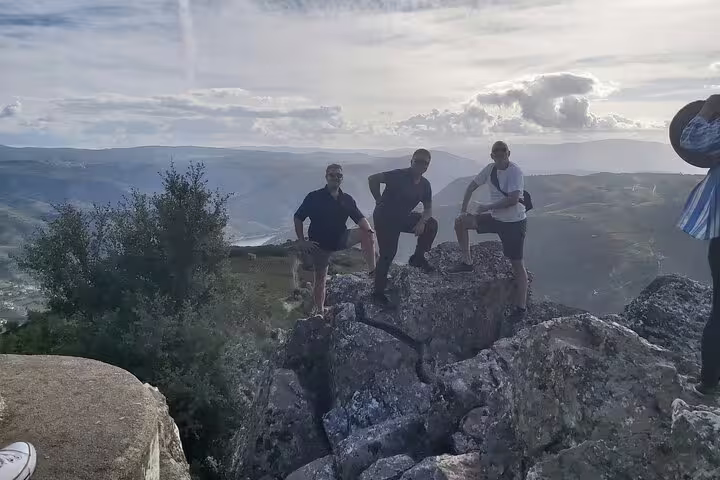 Adventurous tourists standing on rocky cliffs with panoramic views of Douro Valley, showcasing the thrilling wine tour experience.