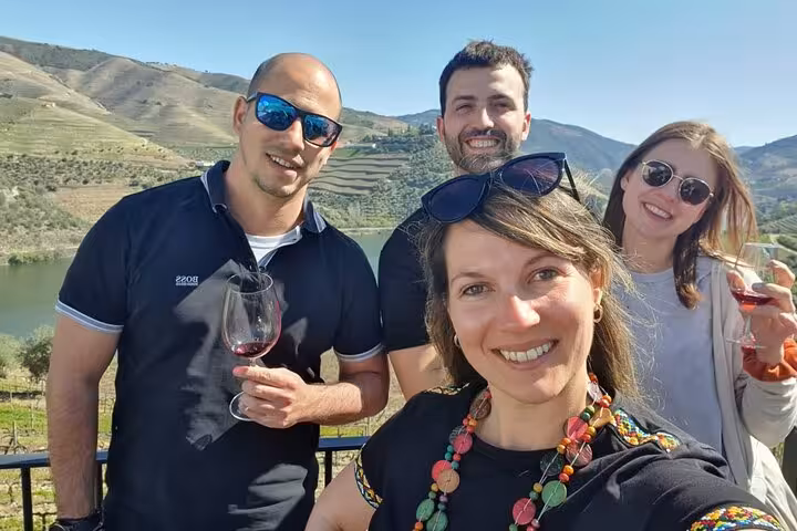 Private group Douro Valley wine tour guests tasting local red wine with river and terraced vineyards behind