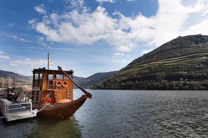 Scenic Douro River with traditional boat and terraced vineyards on a sunny day in Portugal's Douro Valley.