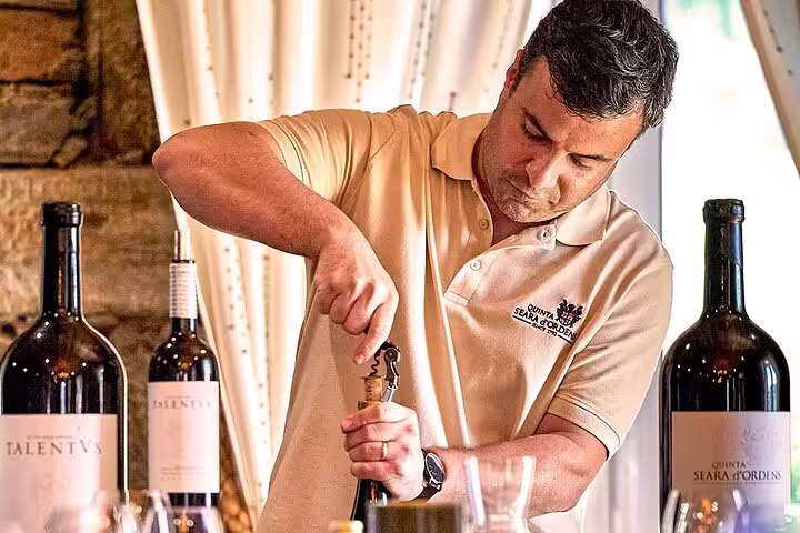 Winemaker opening a bottle during a Douro Valley wine tasting tour with large wine bottles on the table.