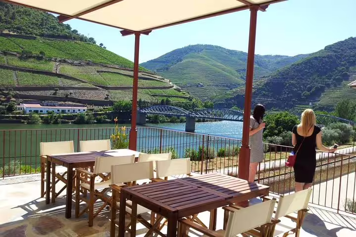 Scenic terrace view over the Douro Valley with dining tables and two women admiring the vineyard landscape and river.