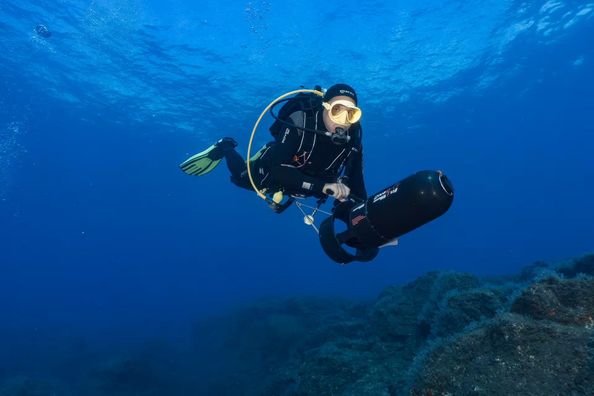 Scuba diver using a DPV scooter gliding above the ocean floor in vibrant blue waters.