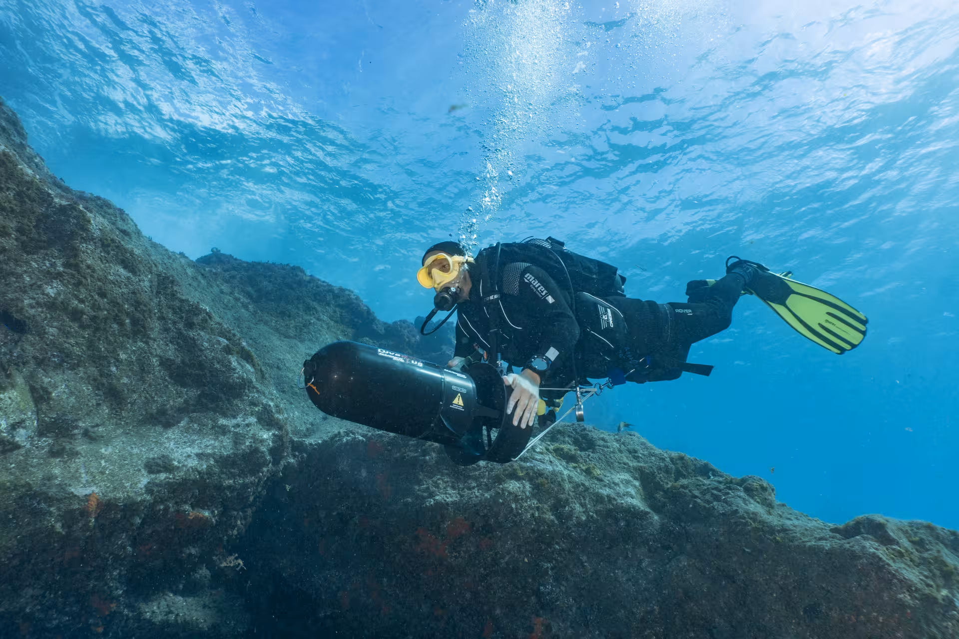 Diver exploring underwater scenery with a DPV scooter in clear blue ocean waters.