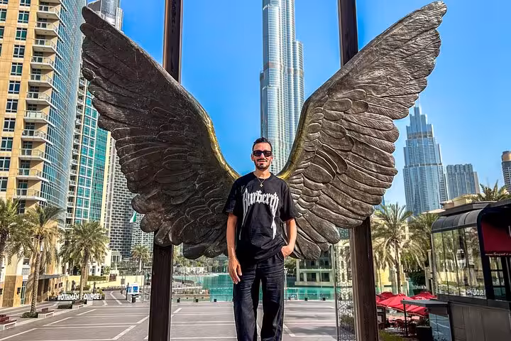 Man standing in front of angel wings sculpture with Burj Khalifa in the background, symbolizing Dubai's modern art scene.