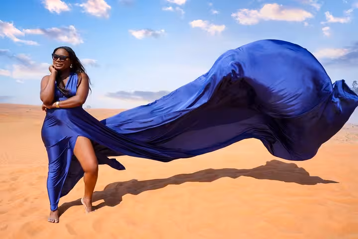 Woman in a flowing blue dress poses in the Dubai desert under a bright sky, capturing the essence of a flying dress tour.
