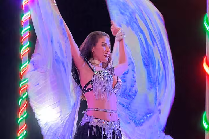 Dubai desert safari belly dancer performing live stage show at BBQ dinner camp with colorful lights