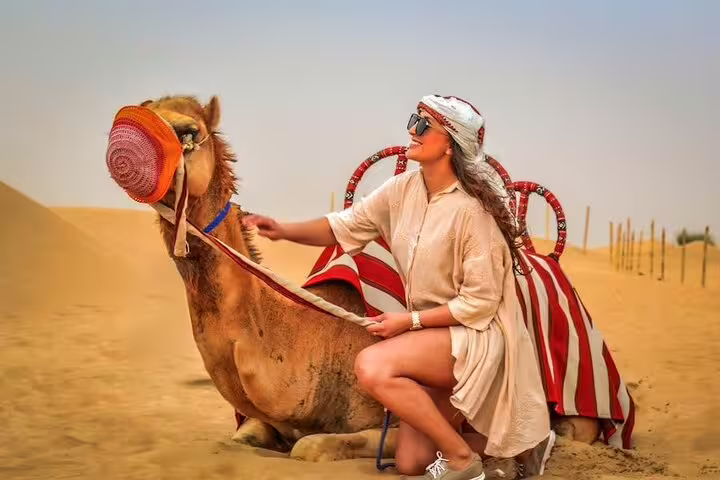 Traveler petting a camel adorned with a colorful blanket in the Dubai desert during a morning safari experience.