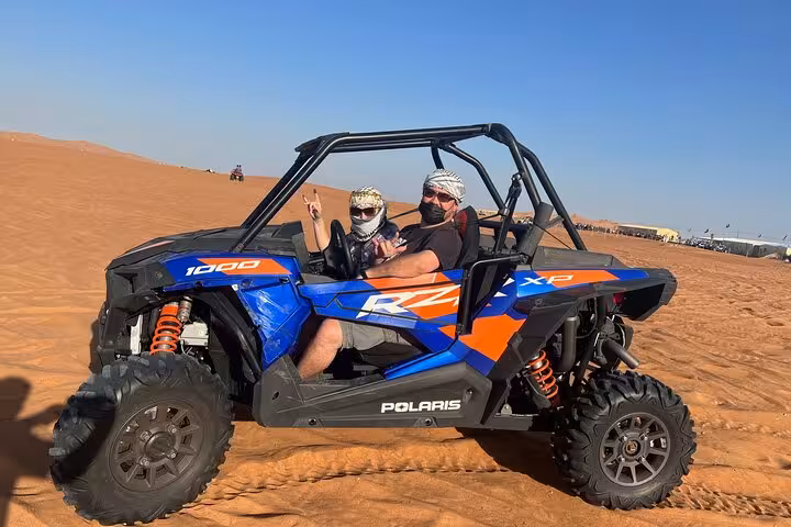 Dubai desert safari quad bike buggy ride, couple driving Polaris RZR across dunes before BBQ dinner