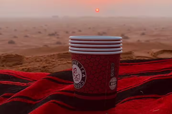 Stacked paper cups on a red blanket against a stunning Dubai desert sunrise, ideal for a refreshing start to a safari.