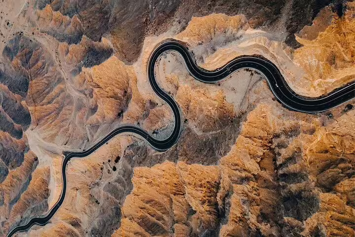 Aerial view of a winding road through arid mountains during the Full-Day Six Emirates Tour from Dubai.