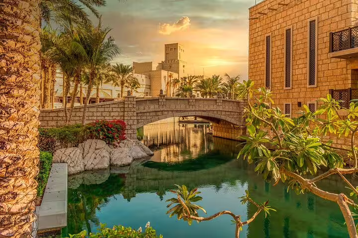 Charming view of Dubai's Madinat Jumeirah with a stone bridge over serene waterways and lush greenery at sunset.