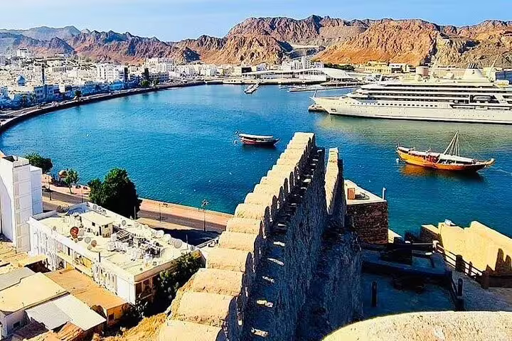 Scenic view of Muscat harbor with yachts and mountains, showcasing picturesque landscapes for travel tours.