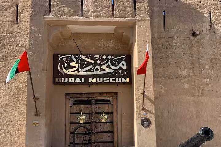 Dubai Museum entrance at Al Fahidi Fort with UAE flags, heritage stop on Dubai city tour from Ras Al Khaimah