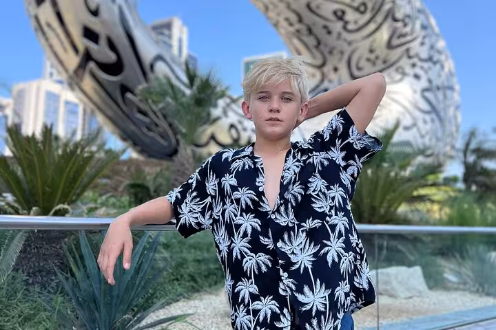 Blonde boy posing in front of the futuristic Museum of the Future in Dubai, showcasing modern architecture.